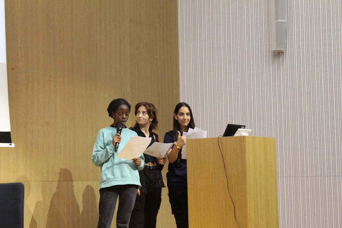 Trois apprenties chercheuses devant un pupitre, lors de la restitution orale de leurs recherches